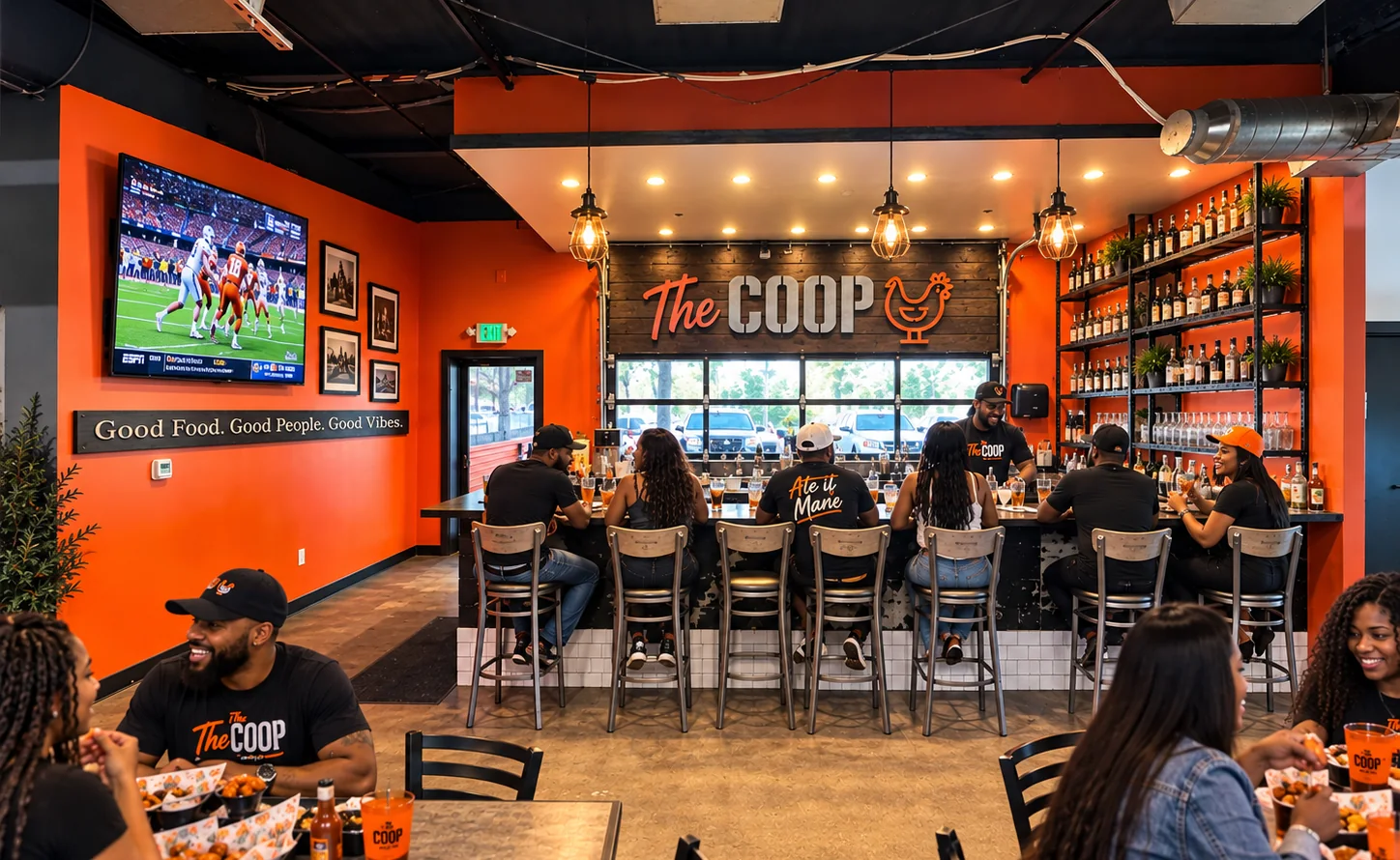 Guests gathering at The COOP bar beneath the restaurant sign, with sports on TV and food at the tables